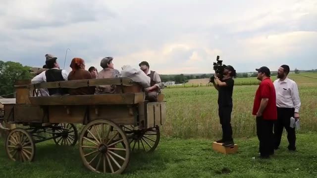 operator on a riser filming the wagon, period actors and crew watching